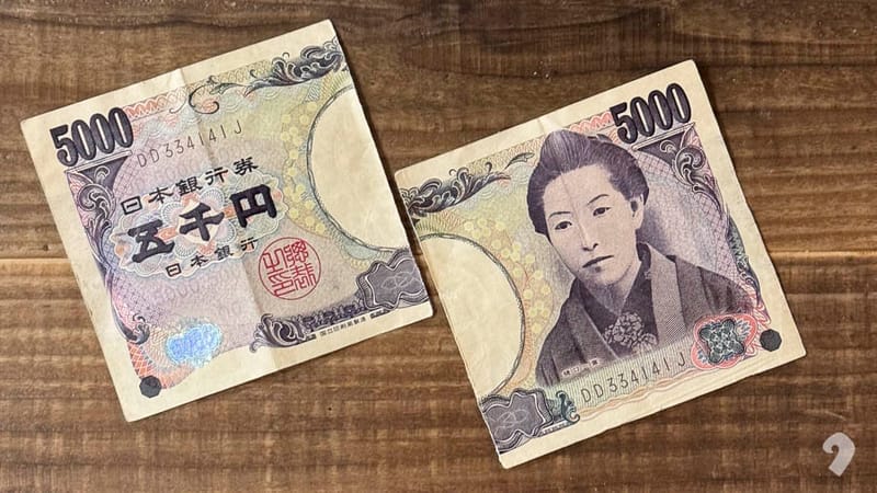兩半撕裂的日幣 5,000 元鈔票（印有樋口一葉像）拼放在木桌上。